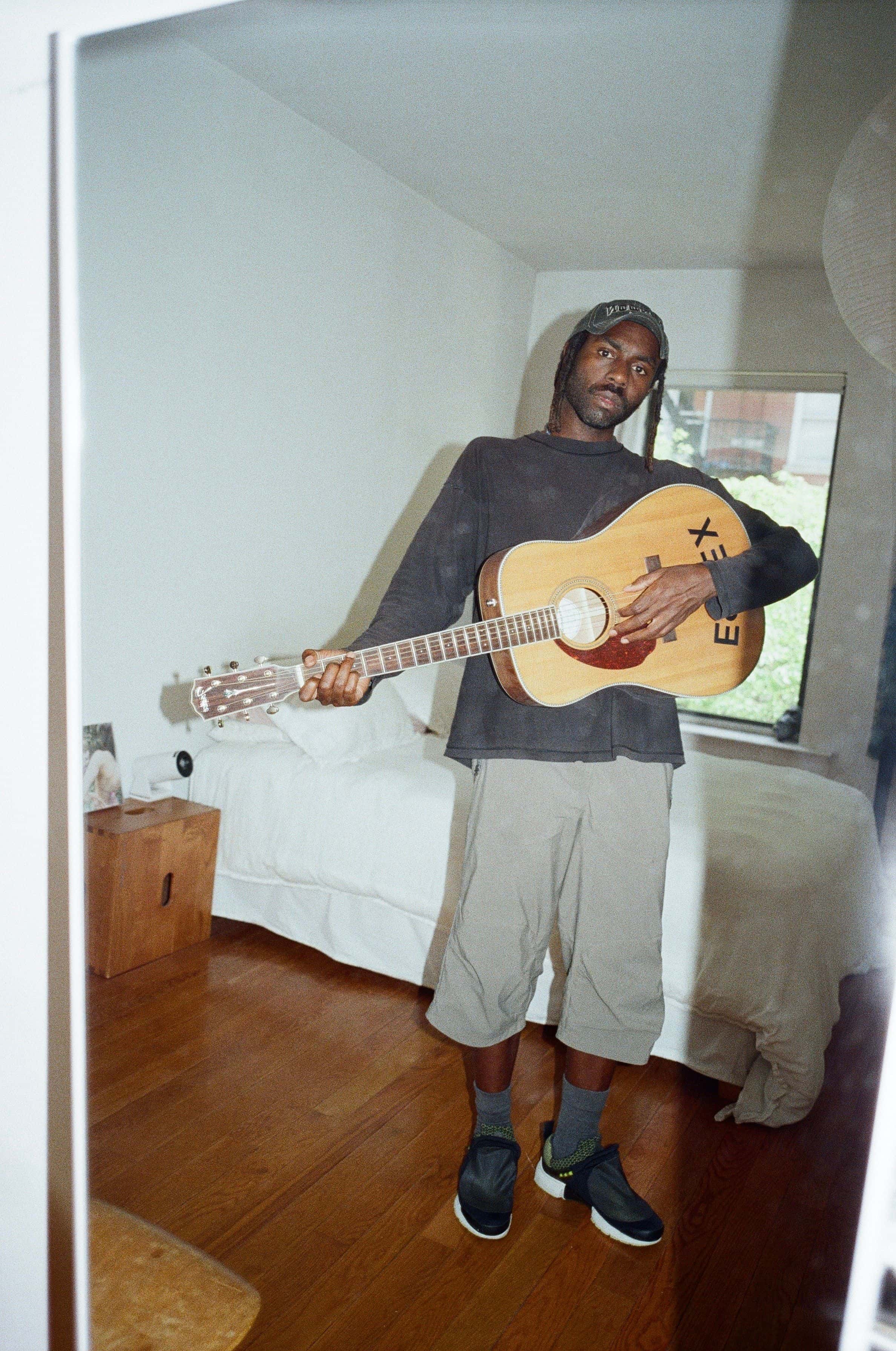 Artisten Blood Orange spiller gitar på soverommet