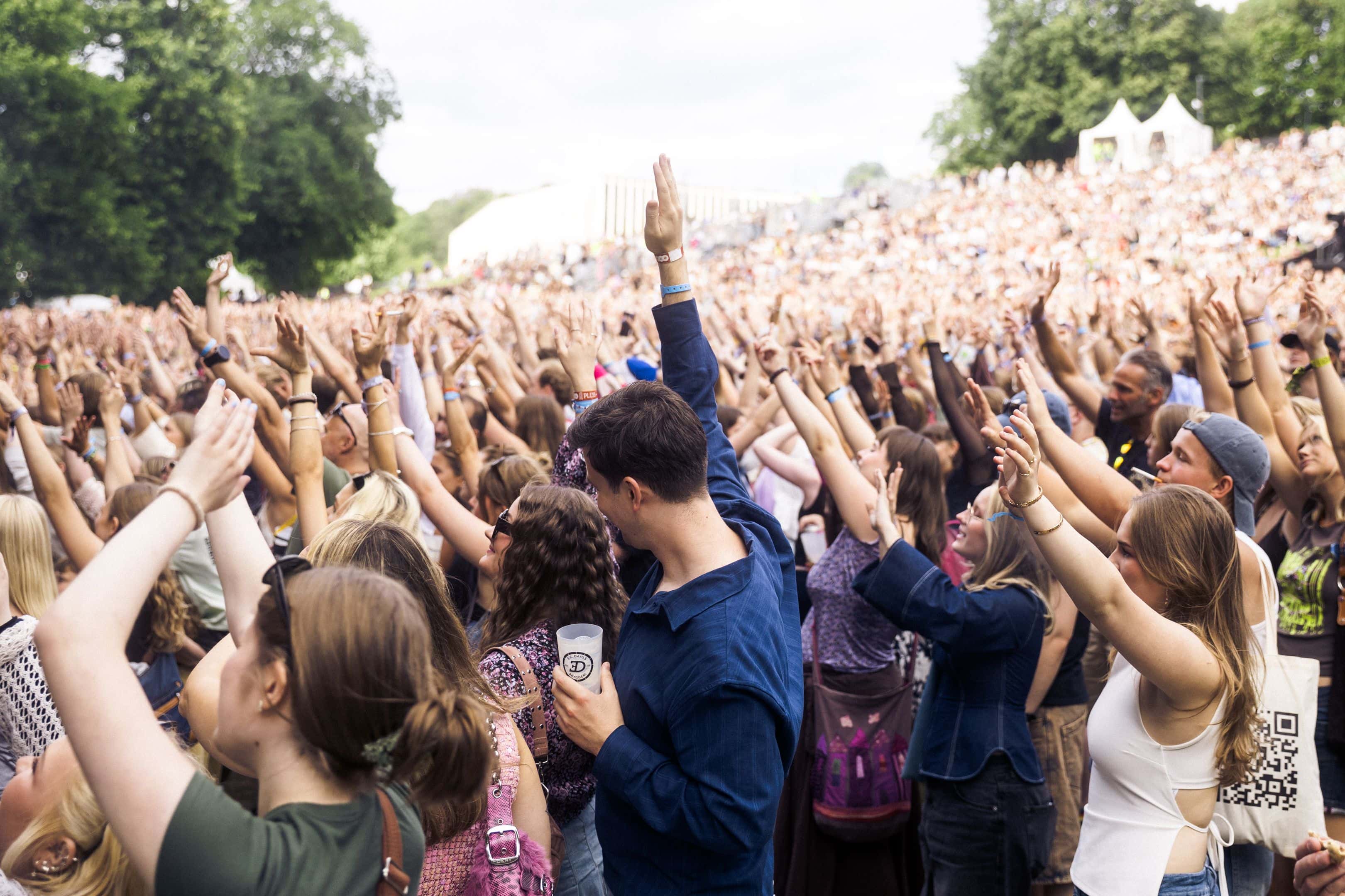 Et samlet publikum løfter armene i Tøyenparken