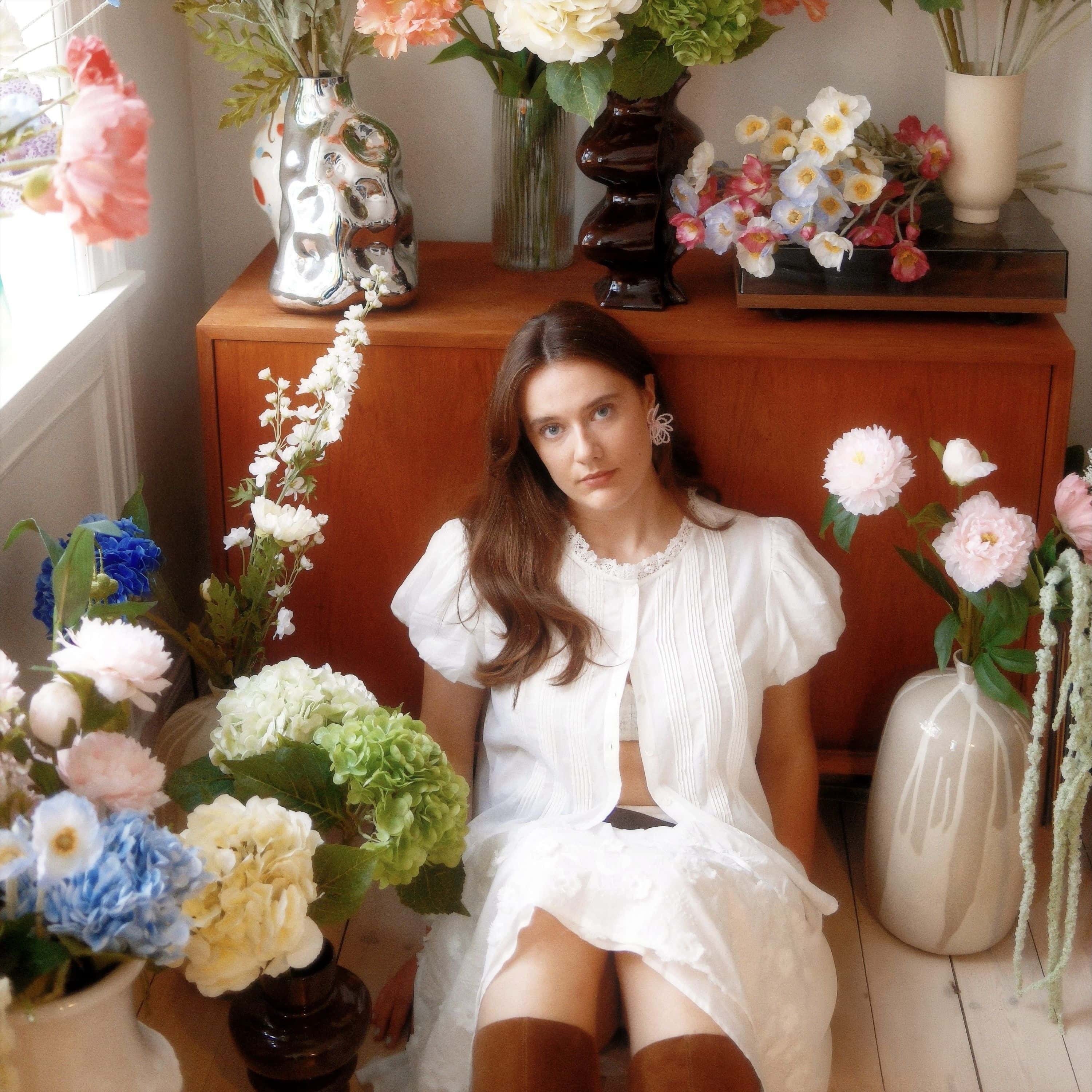 Den norske artisten May i ei stue full av blomster