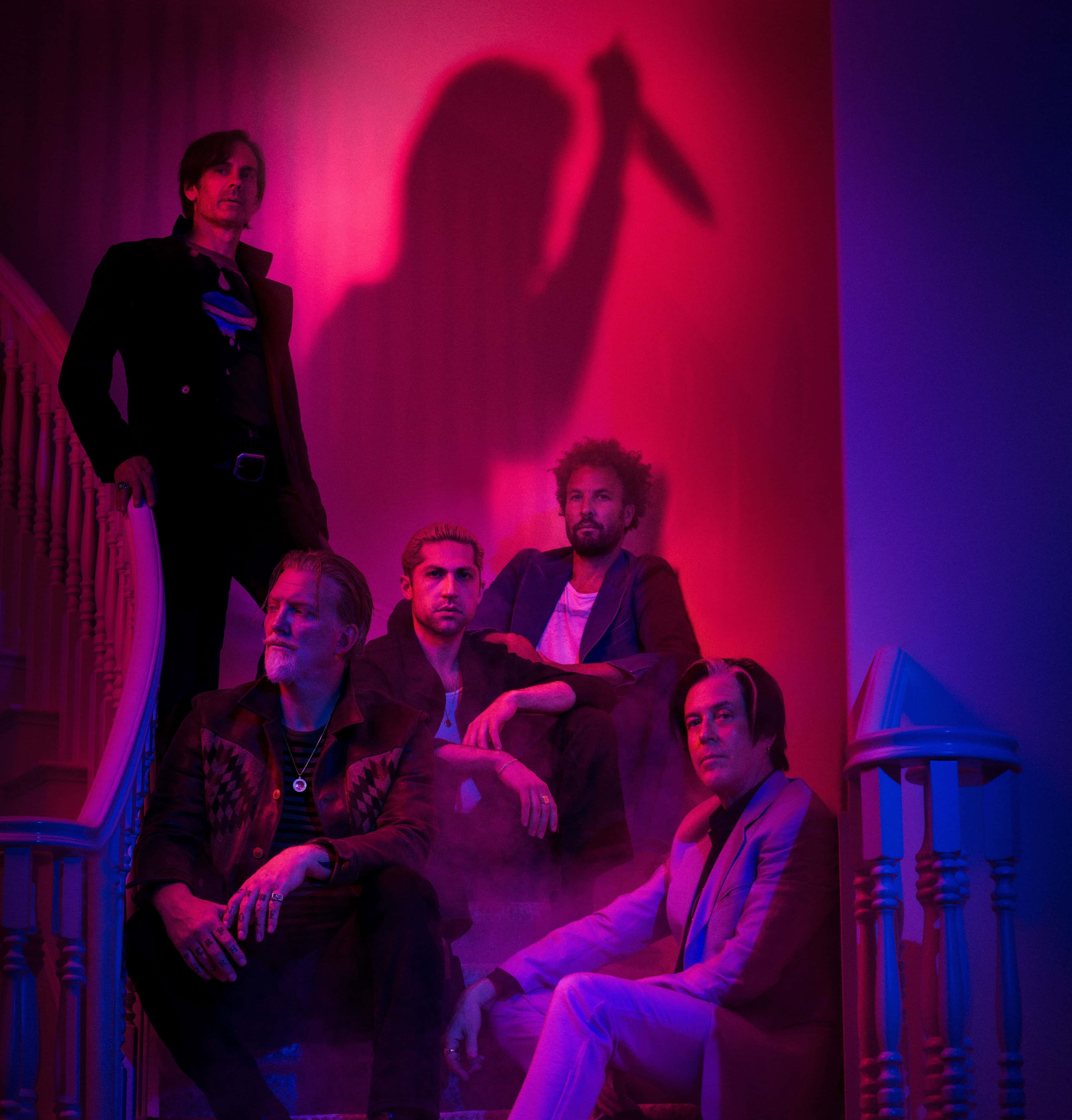Det amerikanske bandet Queens of the Stone Age venter i ei trapp, med uhyggelig skygge bak