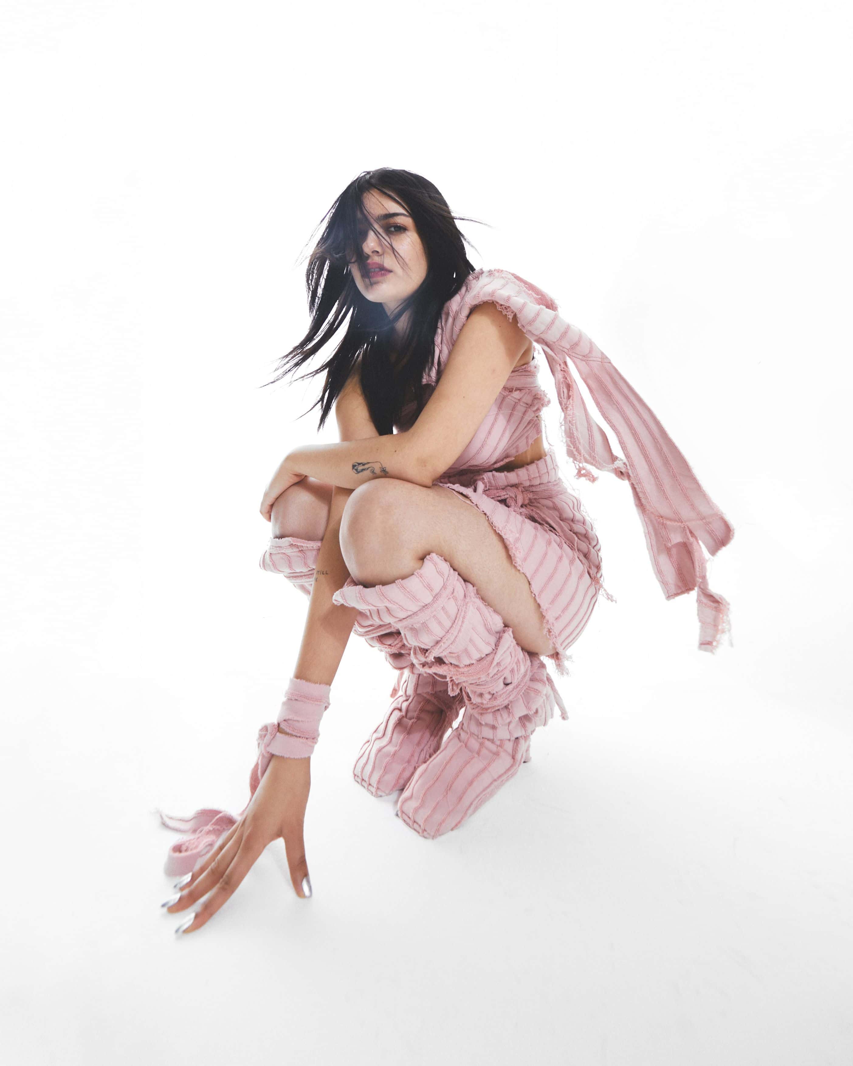 Foto av artisten yunè pinku på huk, iført rosa klær